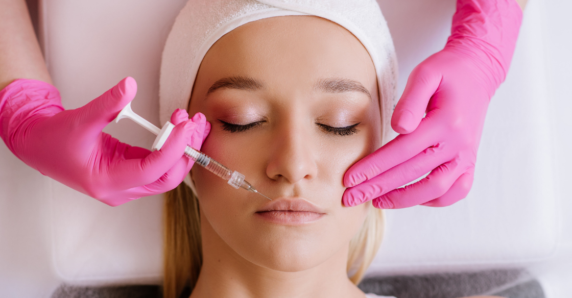 doctor with pink gloves injecting filler in face of young woman