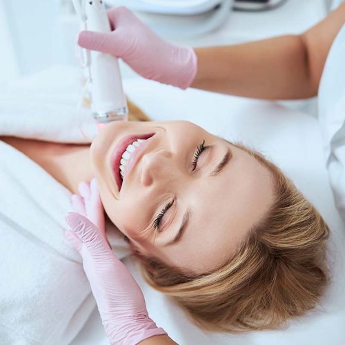 Top view of a joyous woman being treated for neck lines by a qualified cosmetologist